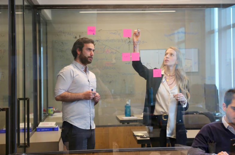Consultores trabajando frente a una pizarra de vidrio con notas